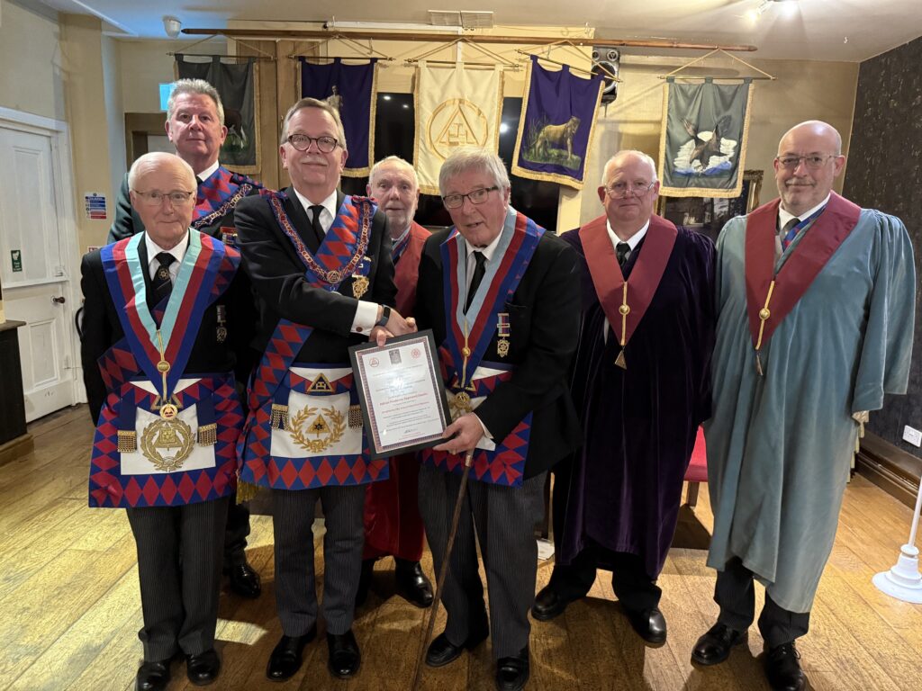 adrian davies, a royal arch mason, being presented with a 50th anniversary certificate form the 2nd provincial grand principal with a number of other royal arch masons around them.