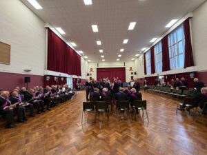 companions seated in a hall ready for a meeting to start