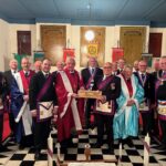 a group of royal arch masons in regalia with the companion in the middle holding the travelling sceptre as he presents it to another companion