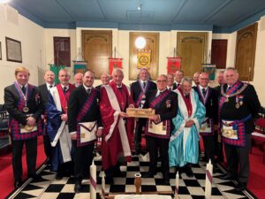 a group of royal arch masons in regalia with the companion in the middle holding the travelling sceptre as he presents it to another companion